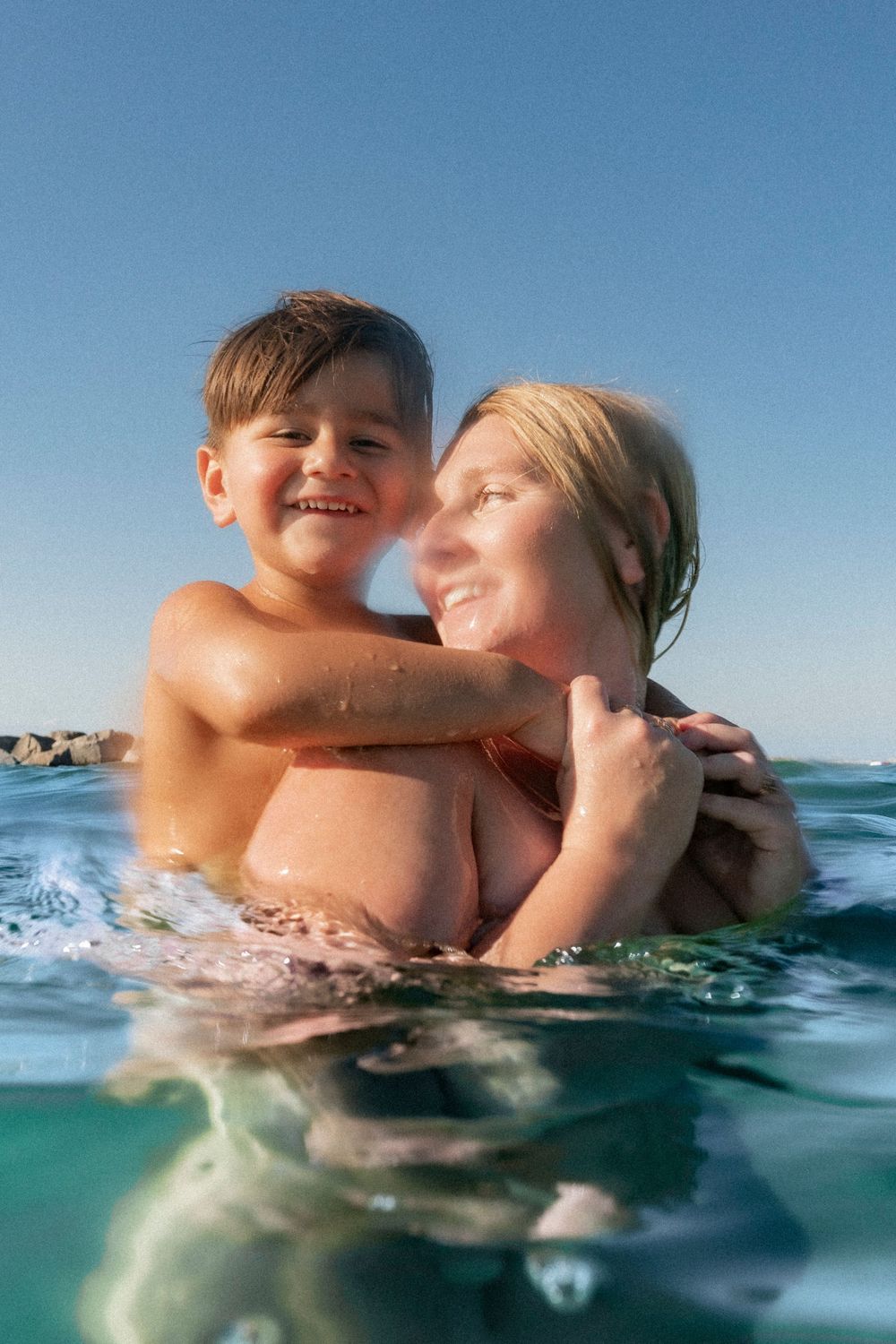 A joyful family enjoying an underwater photoshoot at the Destin Jetties, surrounded by clear emerald water and bright skies.