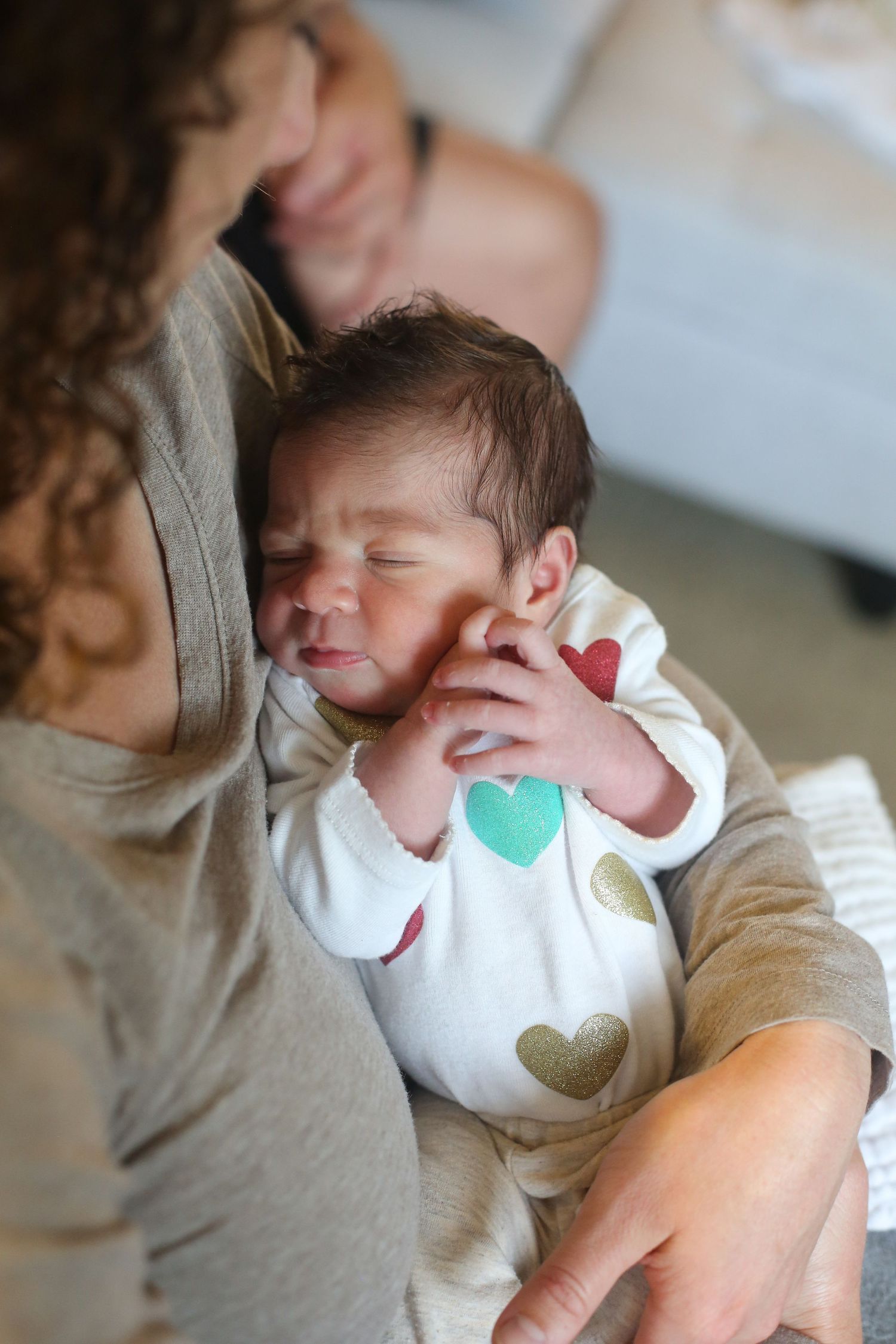 Newborn in heart-patterned onesie snuggles close in candid moment.