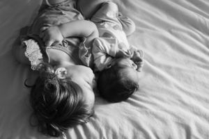 Black and white overhead shot of two young children lying together on bed.
