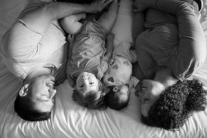 A black and white photograph showing a family lying down together on a bed.