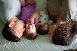 Overhead view of a family lying together on white bedding sharing an intimate moment.