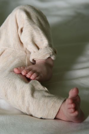 Close-up of tiny baby feet peeking out from cream-colored blanket on white bedding.