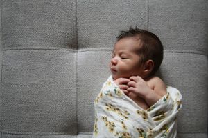 Newborn baby wrapped in floral swaddle resting on gray upholstered surface.