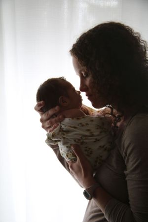 Silhouette of tender moment between parent and baby against bright window background.
