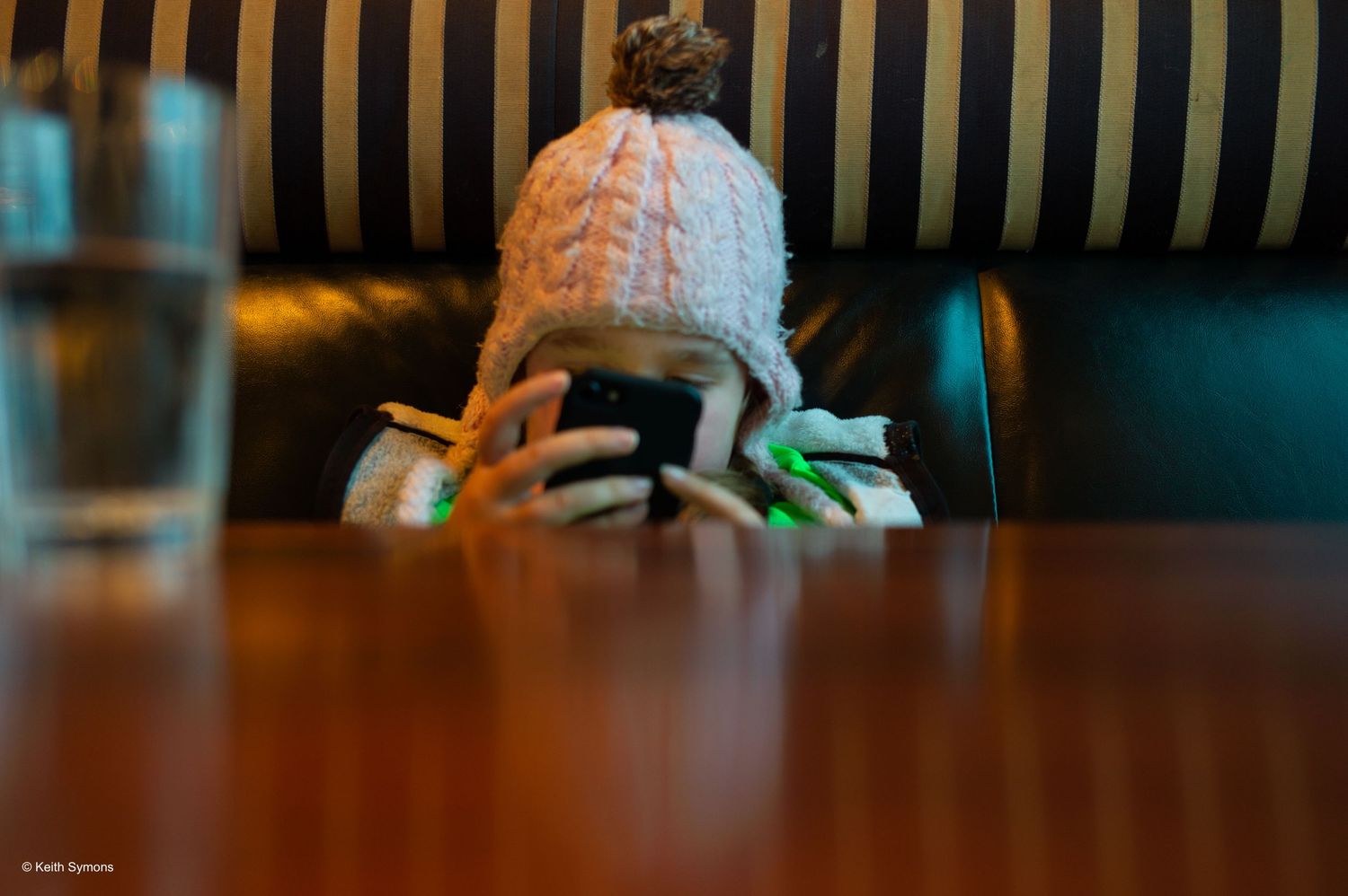 A closeup shot of a person using their phone and wearing a winter hat at a table.