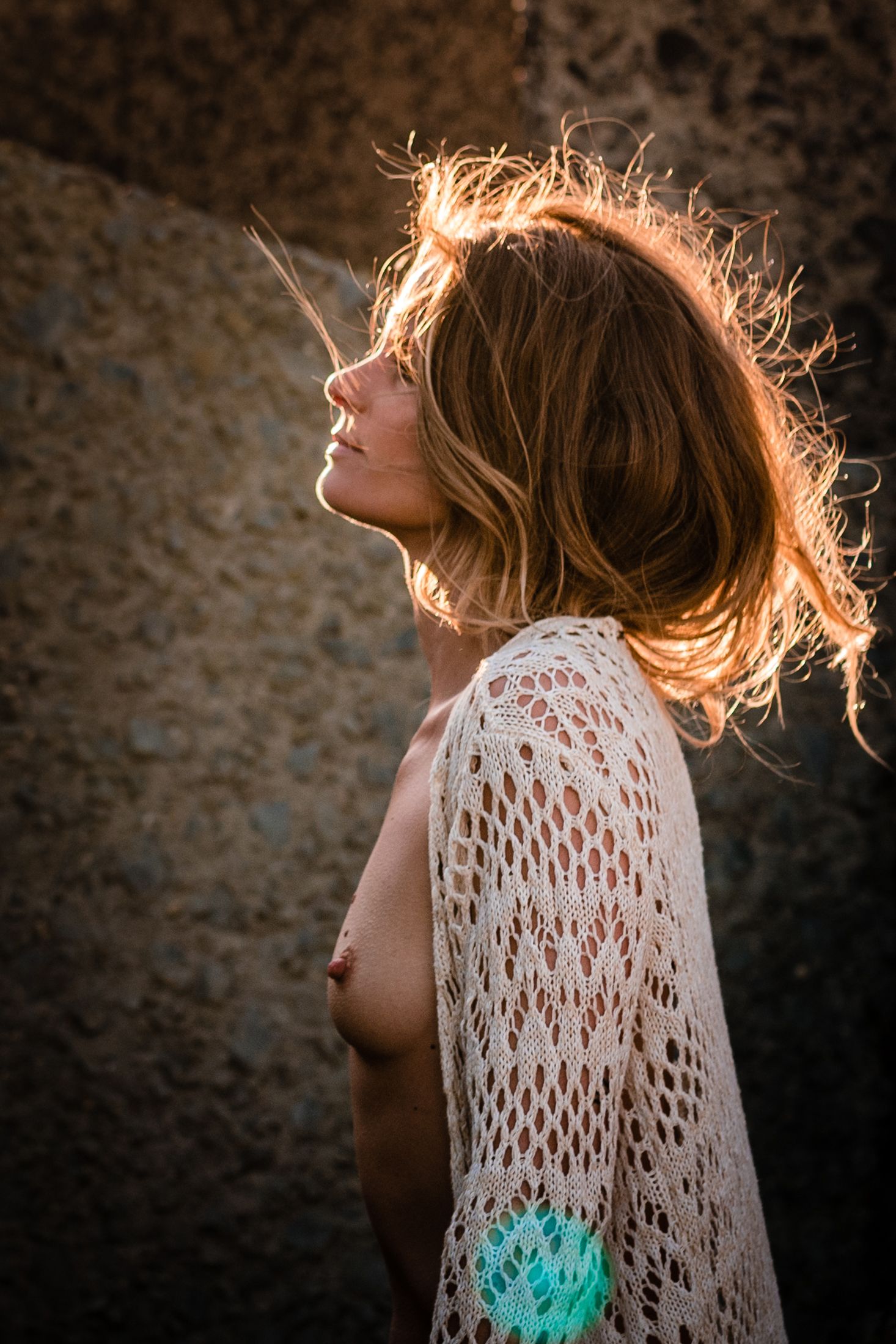 Artistic silhouette of woman in lace garment with backlit hair during golden hour.