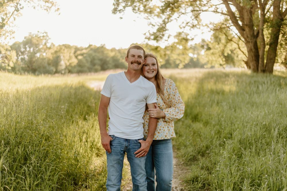 People embracing in a golden summer meadow during sunset, surrounded by tall grass and warm light.