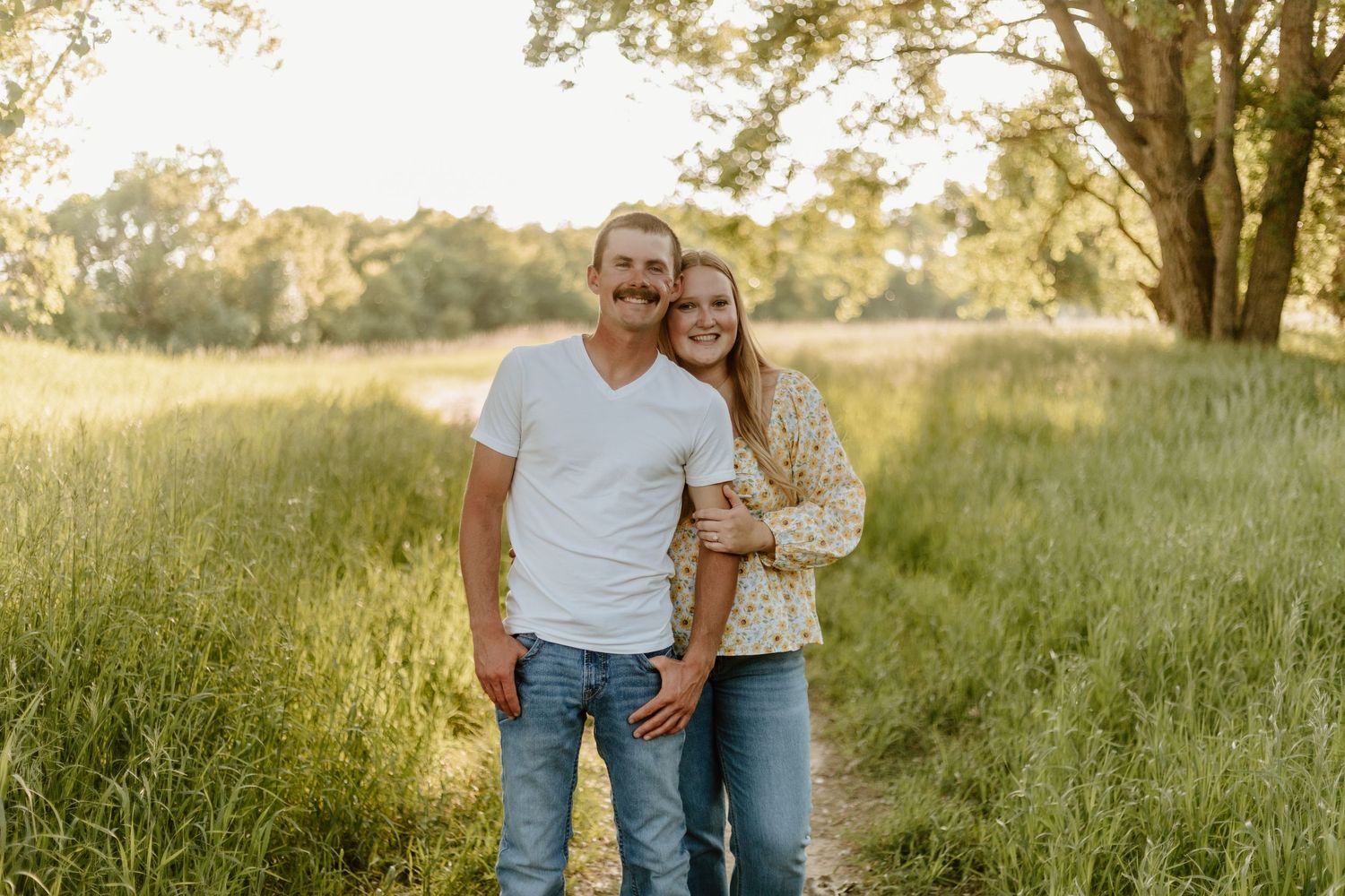 People embracing in a golden summer meadow during sunset, surrounded by tall grass and warm light.