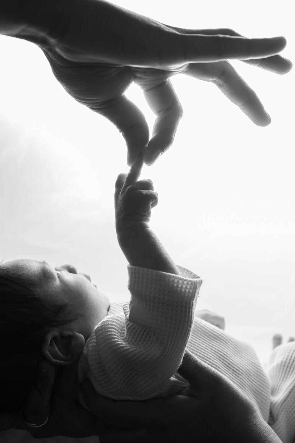 A tender black and white silhouette shows a small child reaching up to grasp an adult's hand against a bright background.