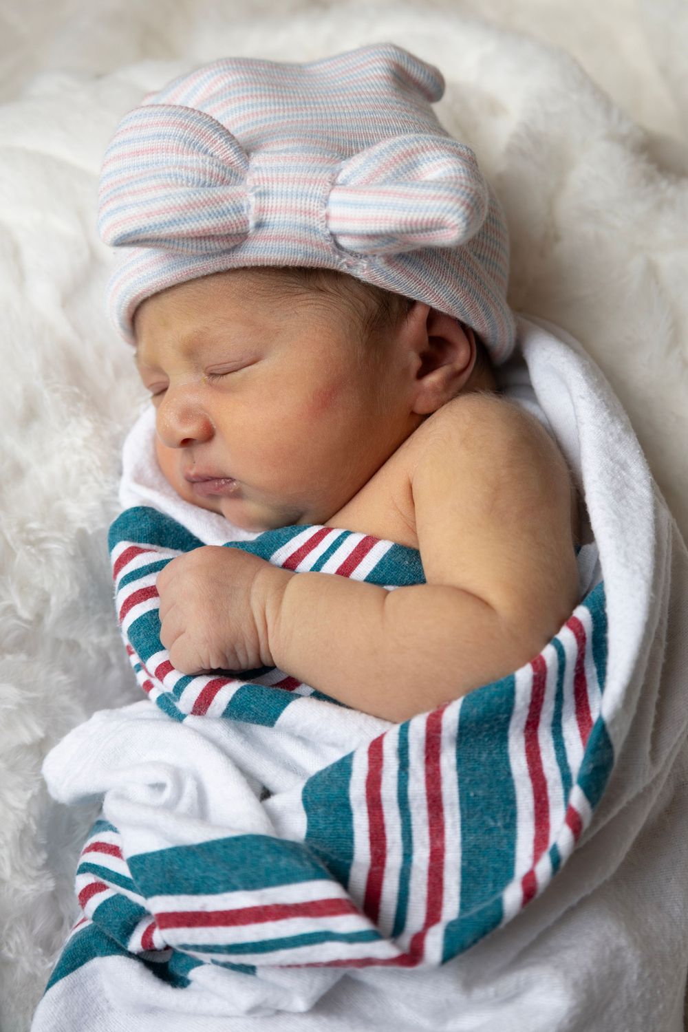 Newborn baby sleeping peacefully in striped outfit and matching hat.
