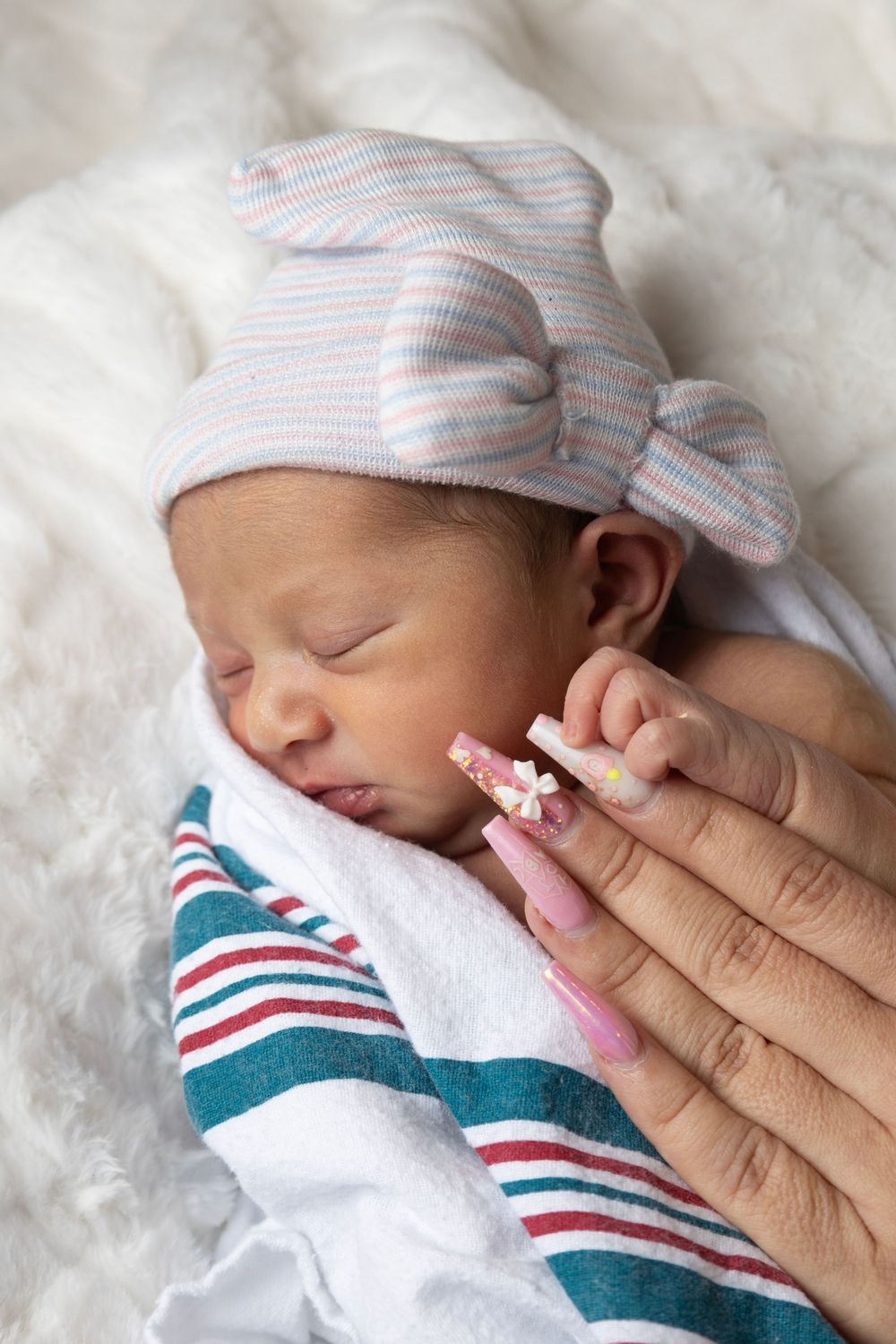 Gentle hand touching sleeping newborn in striped hat and blanket.