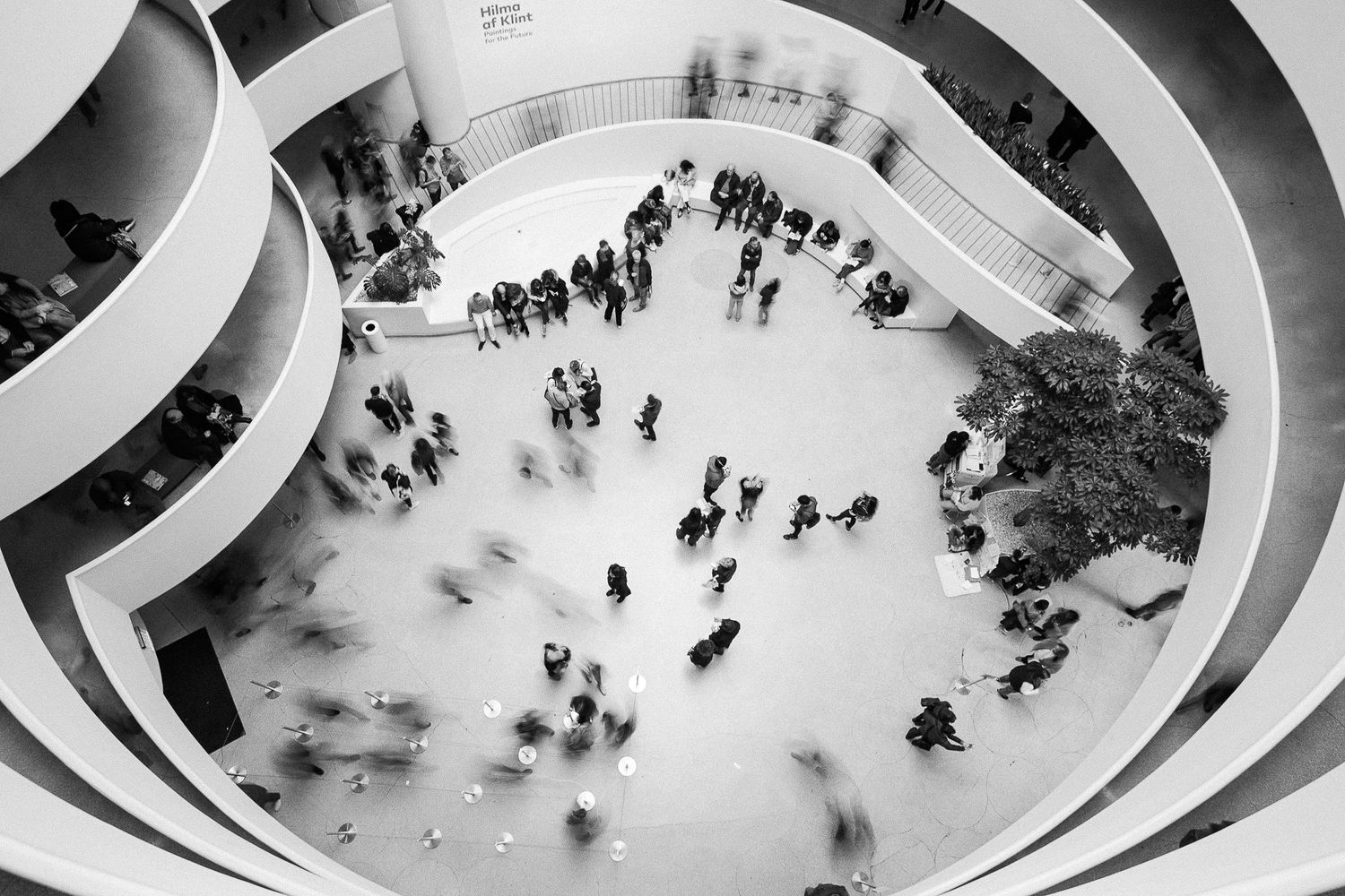 Aerial view of people walking in spiral architecture captured in black and white with motion blur effect.