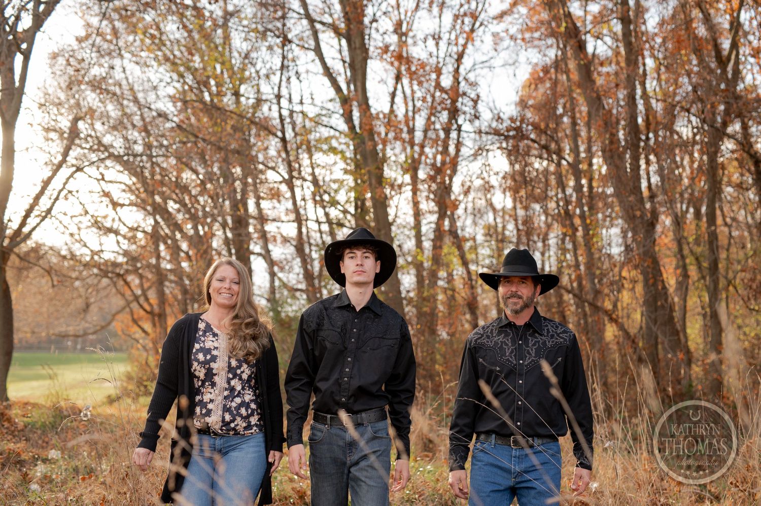 Three people in western wear walking through autumn woods together.