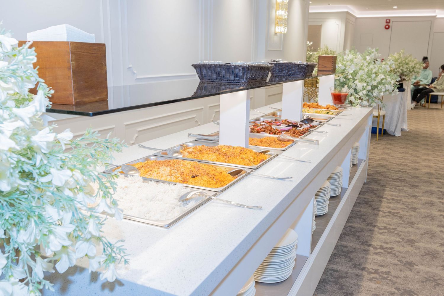 Buffet setup with food warmers and white floral decorations in modern space.