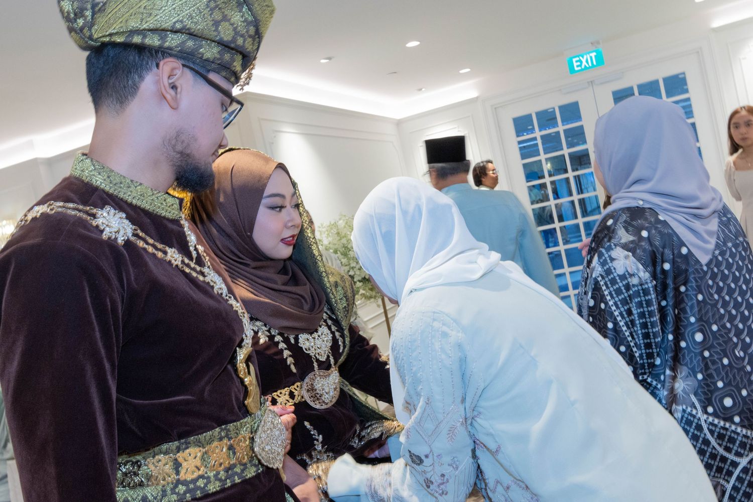 Traditional Malay wedding reception with guests greeting the couple in formal attire.