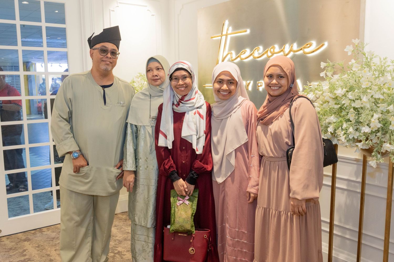 Group photo in modern Malay formal wear standing beneath neon signage.