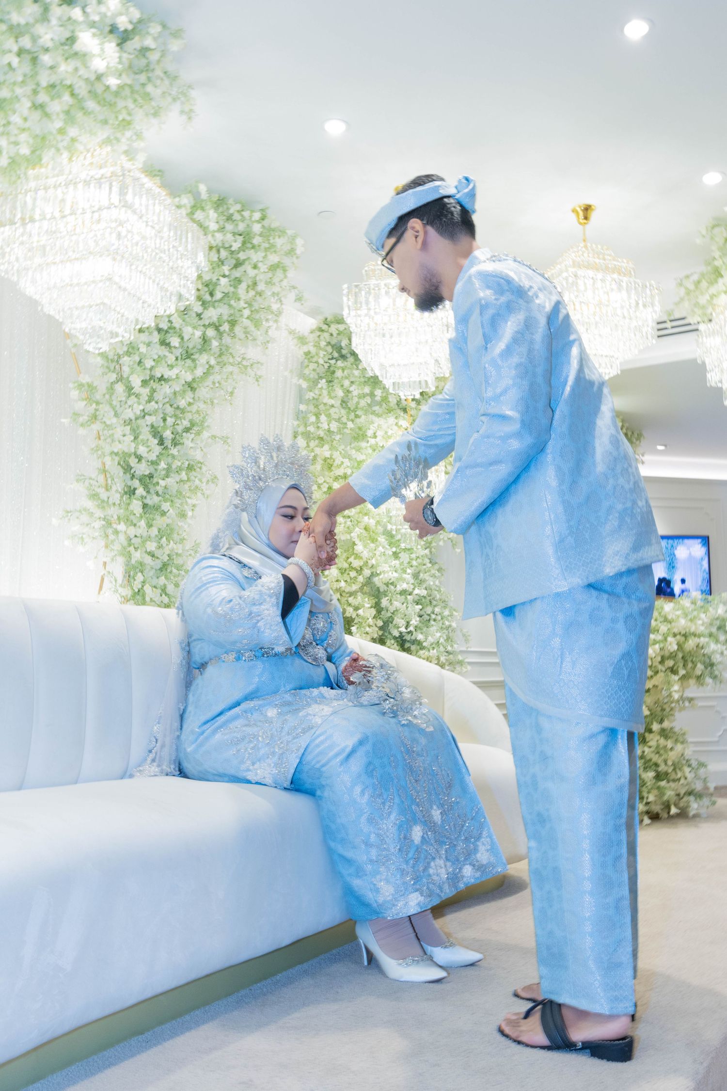 Couple in matching light blue traditional attire sharing a tender moment on a white couch.