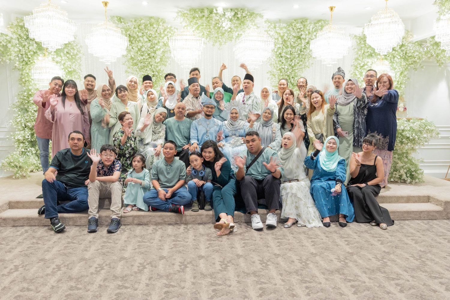 Large group photo of event attendees posing together against floral decorated backdrop.