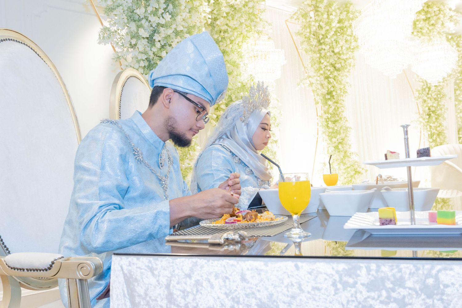 Two people in powder blue attire dining at an elegant table with floral decorations.
