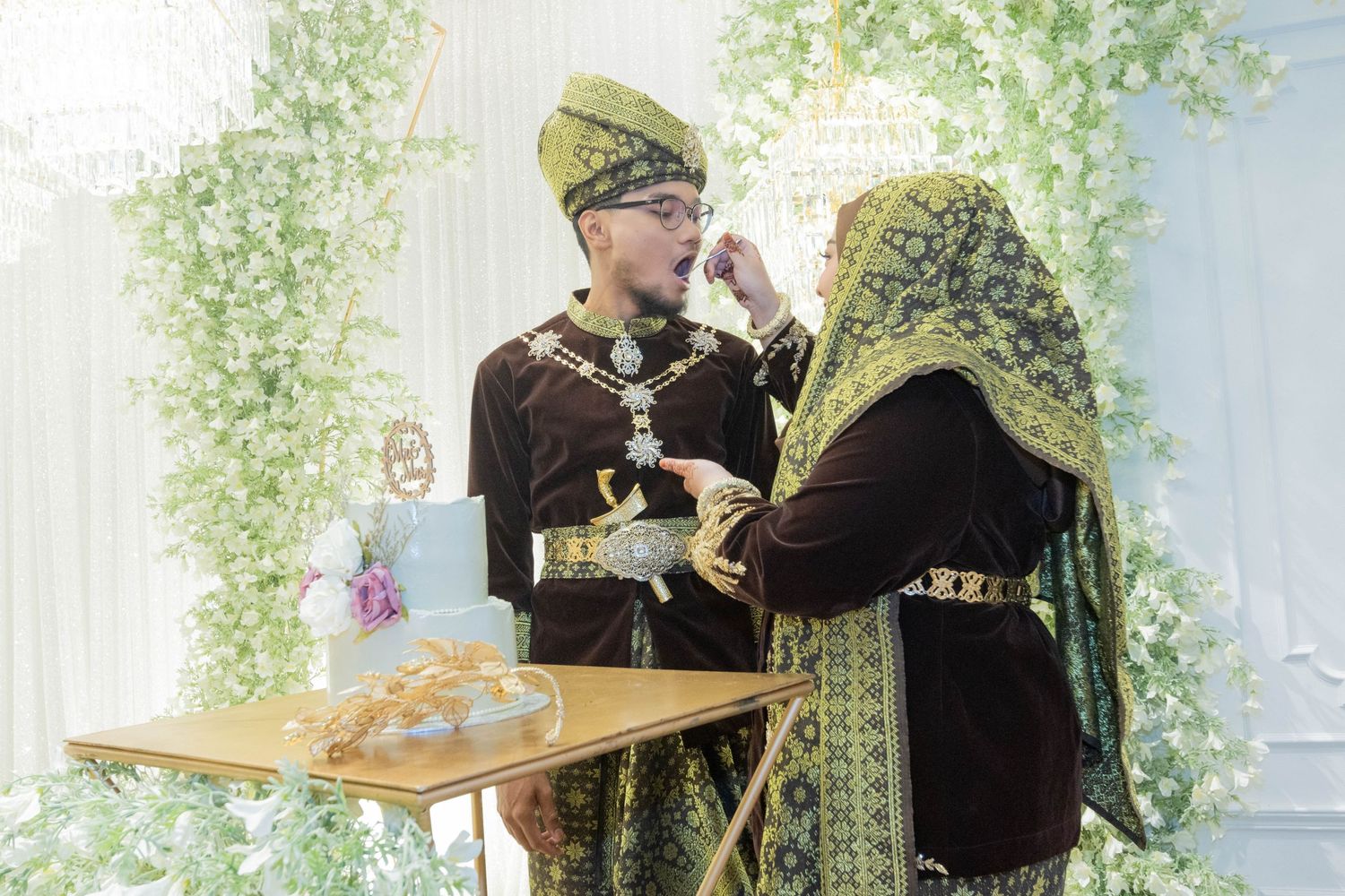 A couple in traditional brown and gold Malay attire sharing a moment during their celebration.