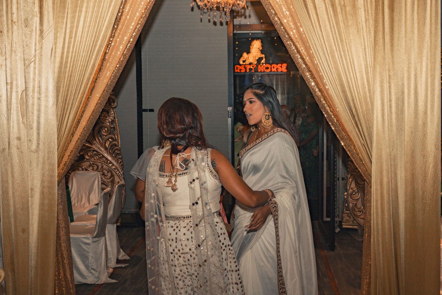 Guests in elegant white dresses stand beneath gold curtains at a formal event.
