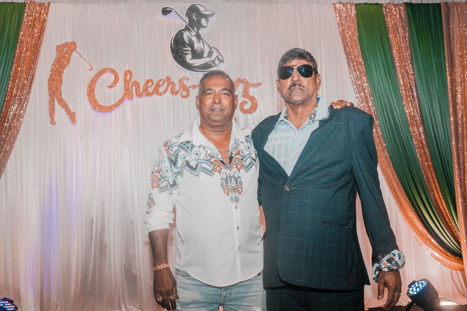 Two people posing at a 75th anniversary celebration with decorative backdrop and event signage.