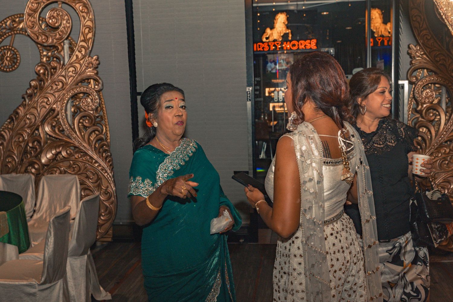 Party guests in formal attire mingling near ornate gold decor at an evening event.