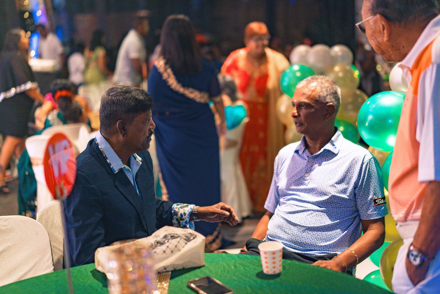 Two people having a conversation at a table during what appears to be a social gathering or event.