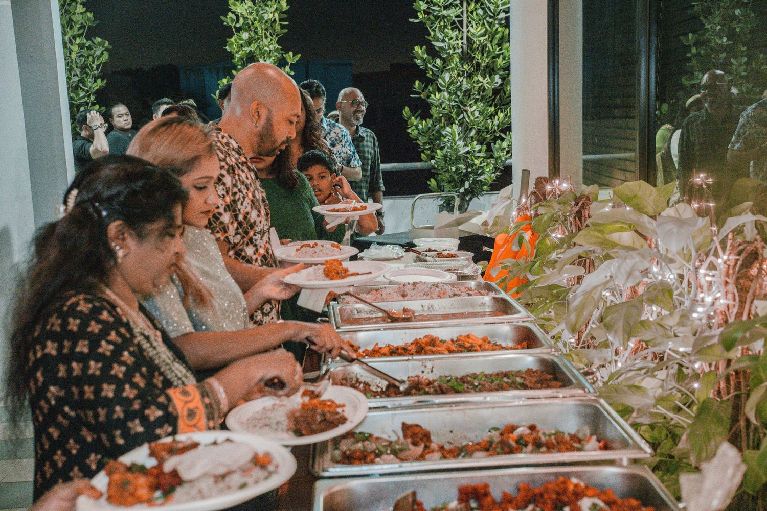 People serving themselves food from a buffet line with multiple dishes and serving trays.