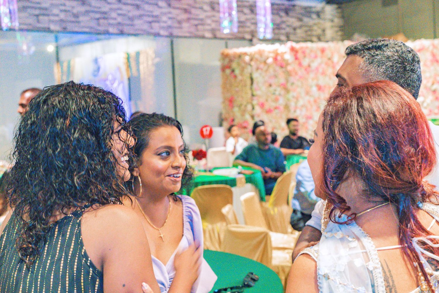 Three women engaged in conversation at a festive indoor event.
