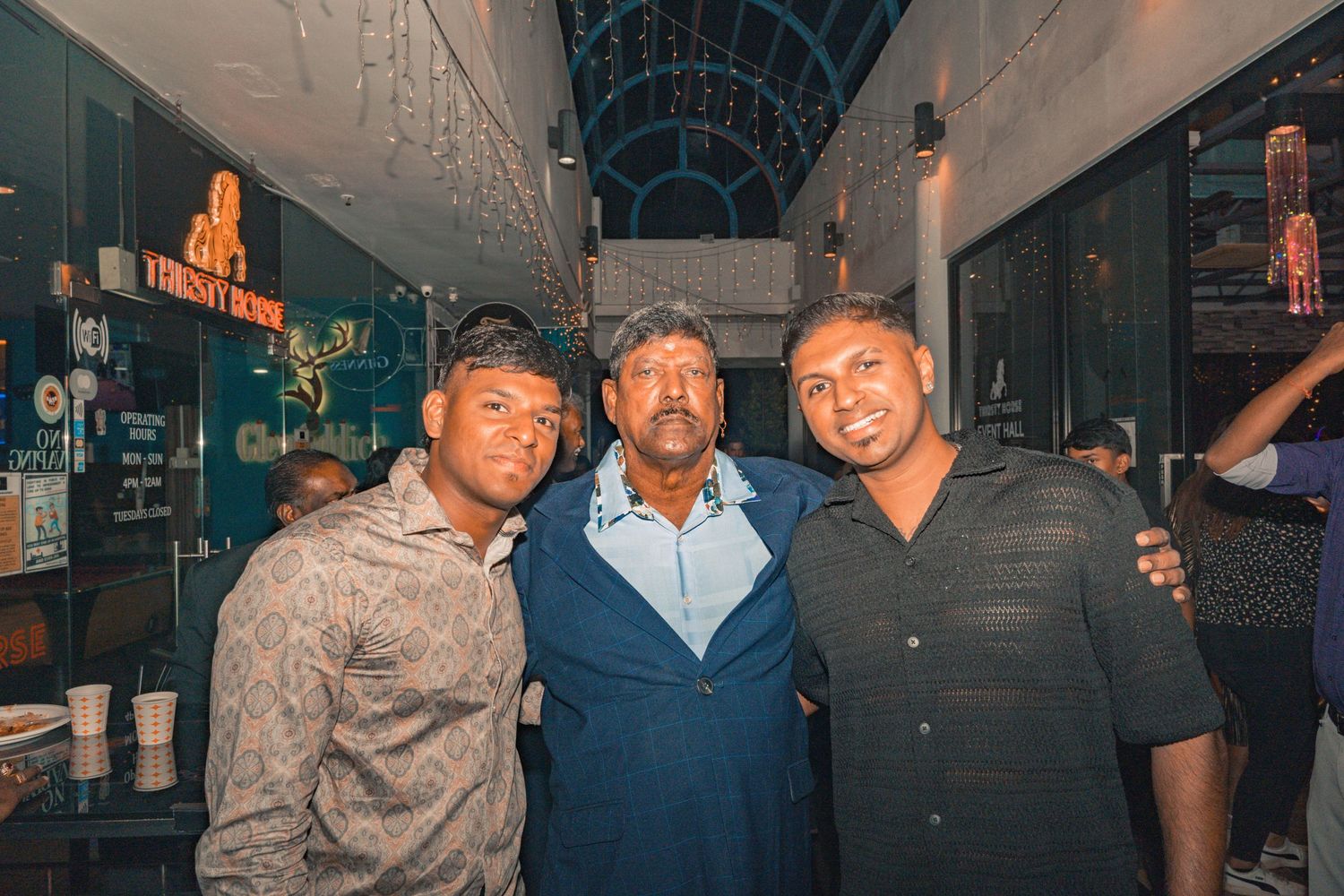 Three individuals posing together at a venue with blue lighting and decorative elements.