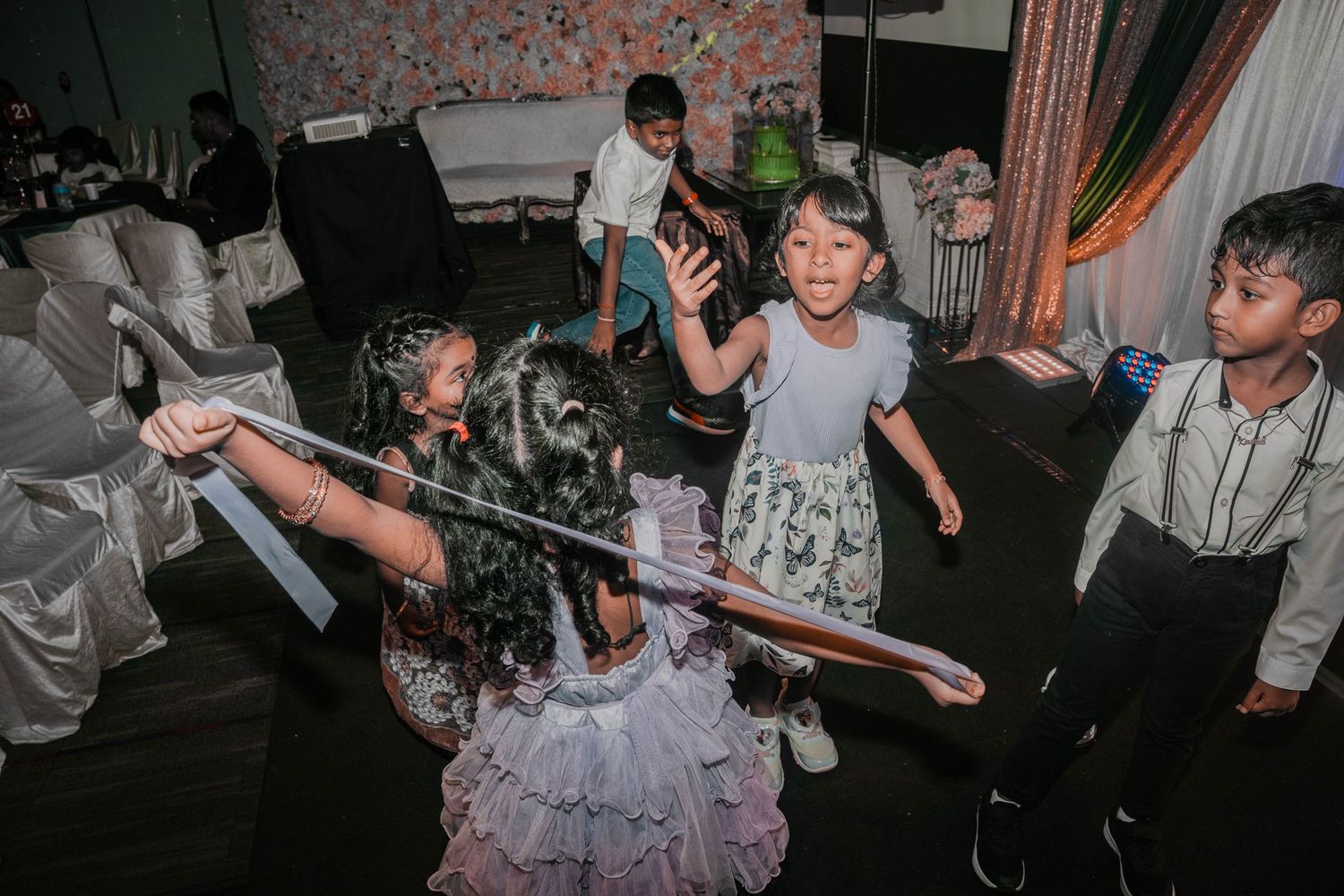 Children playing and dancing at a party with decorative lighting and formal attire.