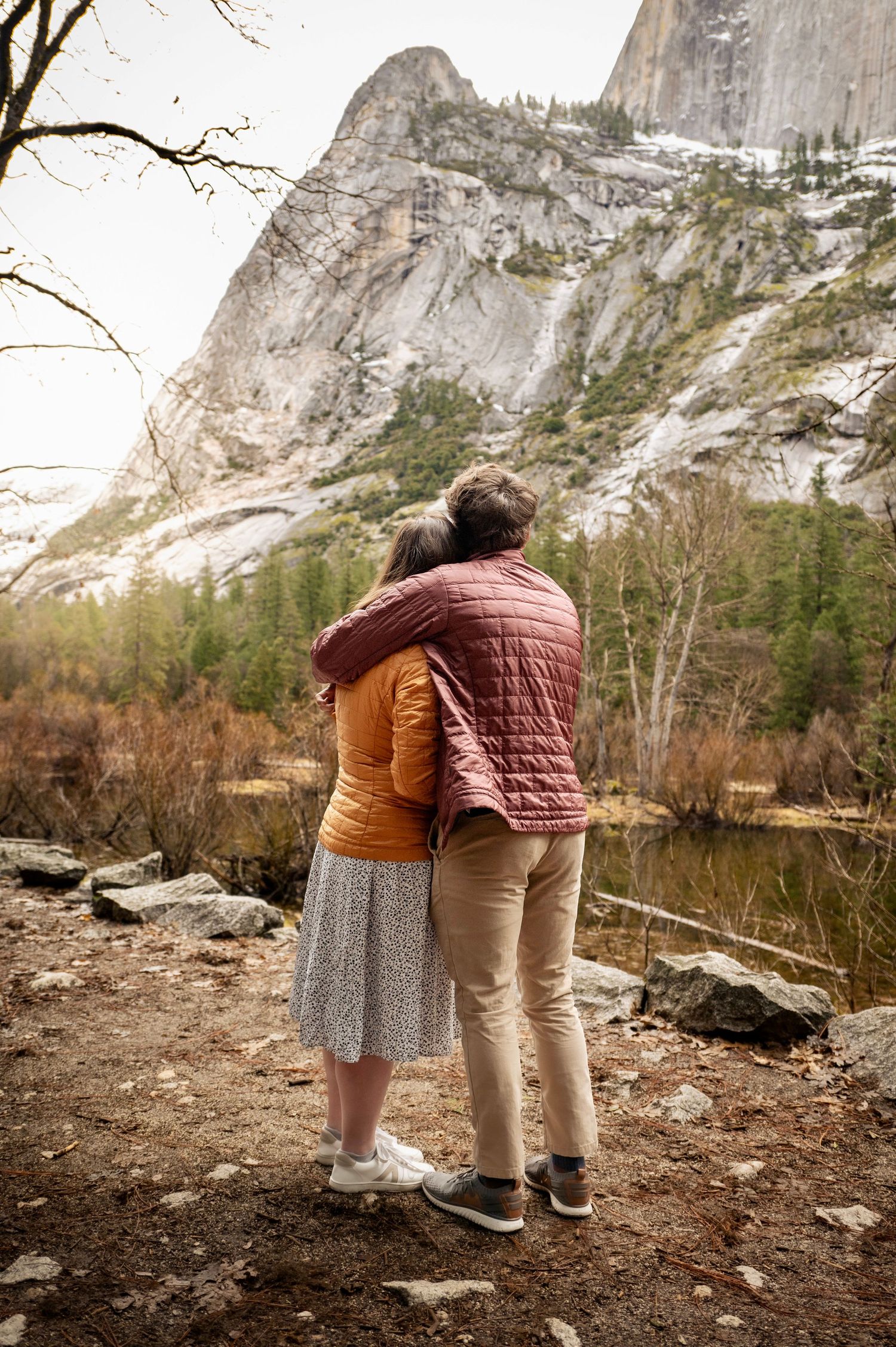 A couple hugging while viewing the cliffs at Mirror Lake, Yosemite, after a surprise proposal and fun hike together