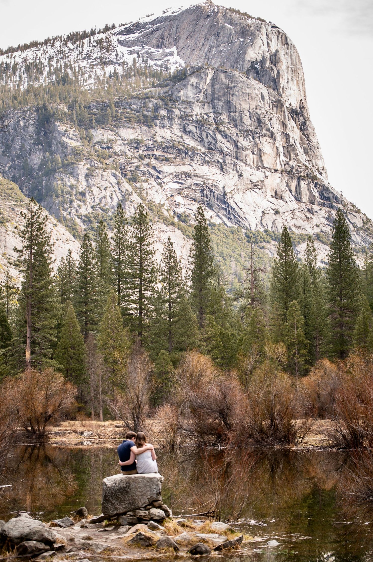 A couple reflected in a cozy snuggle at Mirror Lake, Yosemite, after a surprise proposal and fun hike together
