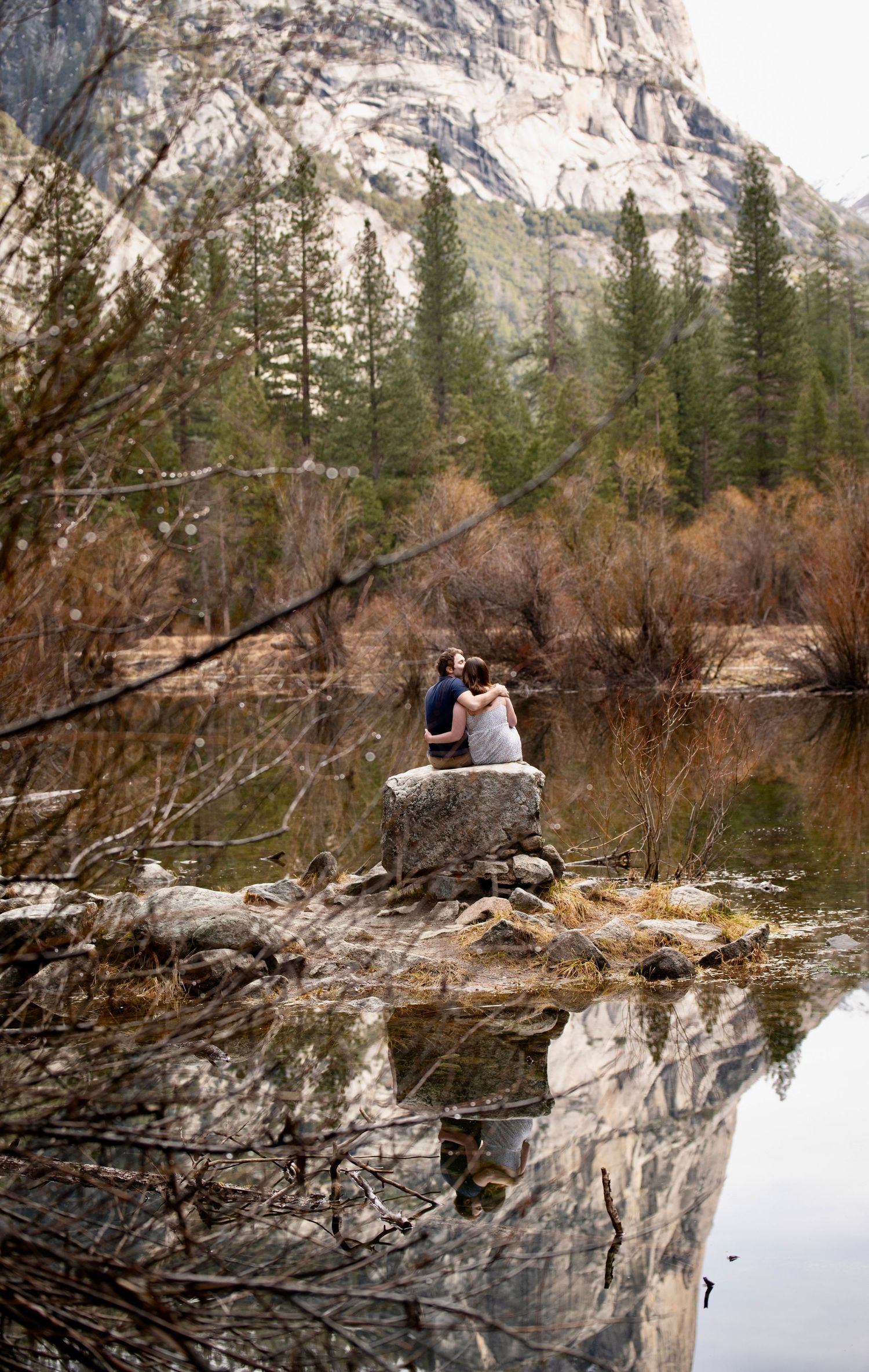 A couple reflected in a cozy snuggle at Mirror Lake, Yosemite, after a surprise proposal and fun hike together