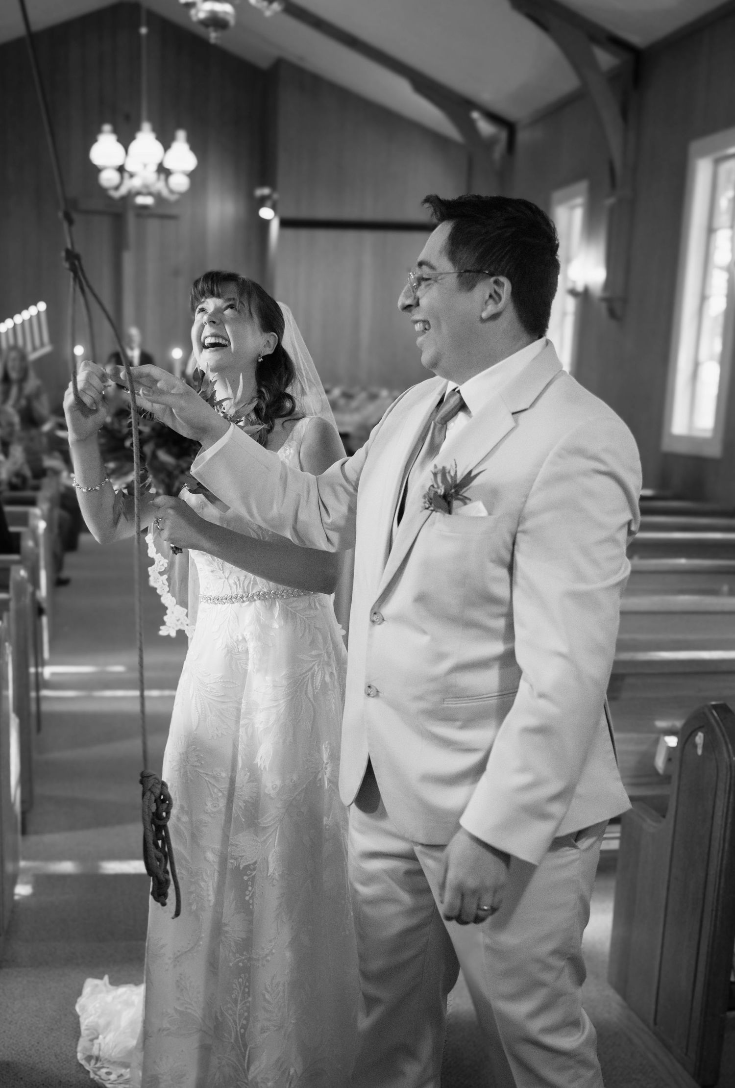 A black and white portrait of a bride and groom ringing the bell after their wedding at Yosemite Chapel