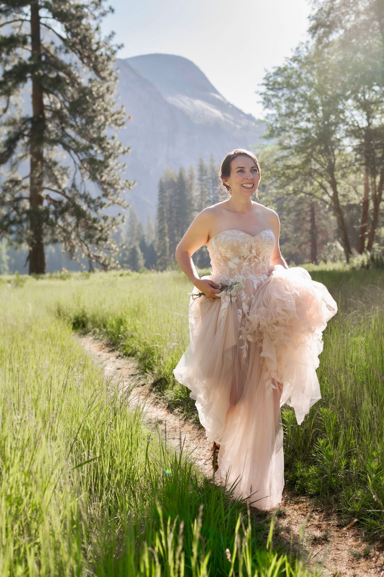 A bride hikes up her dress and runs down a path in Yosemite California