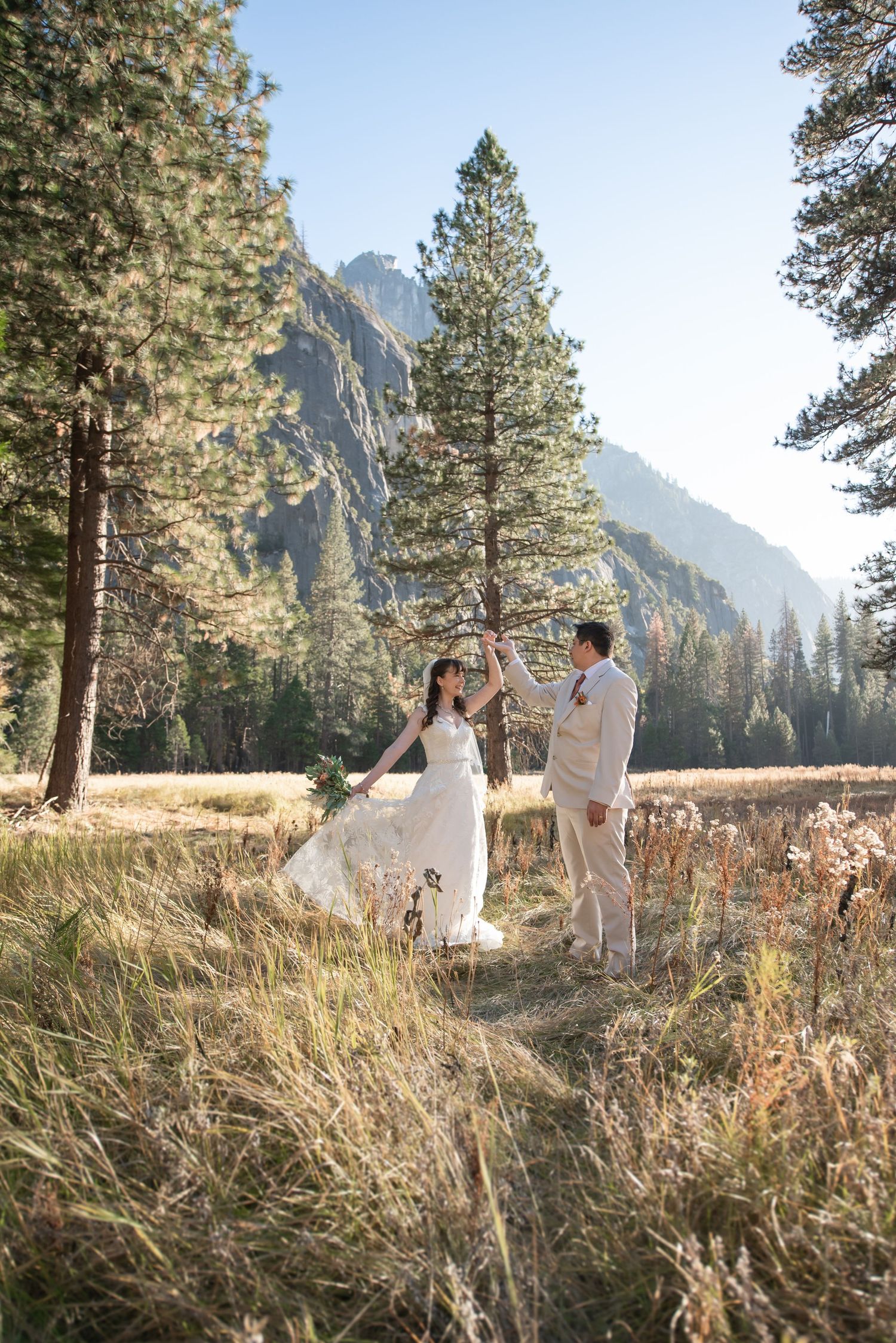 A bride and groom dancing in a meadow full of trees in front of mountains in Yosemite