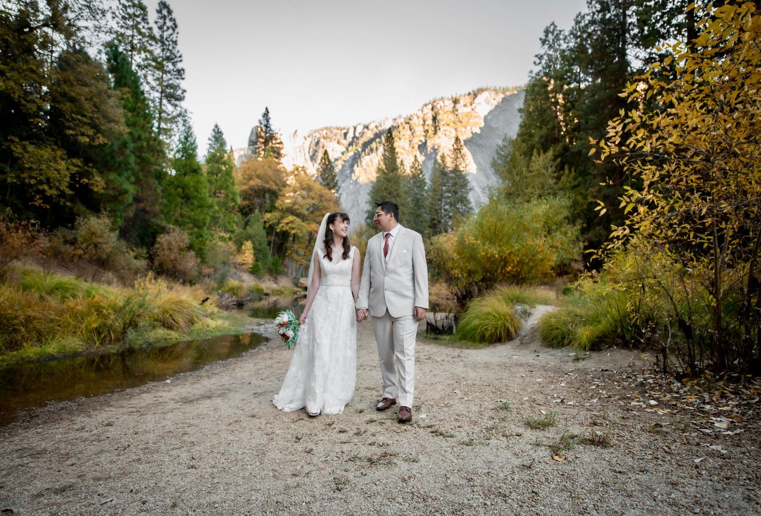 A bride and groom on the sandy banks of a river in Yosemite