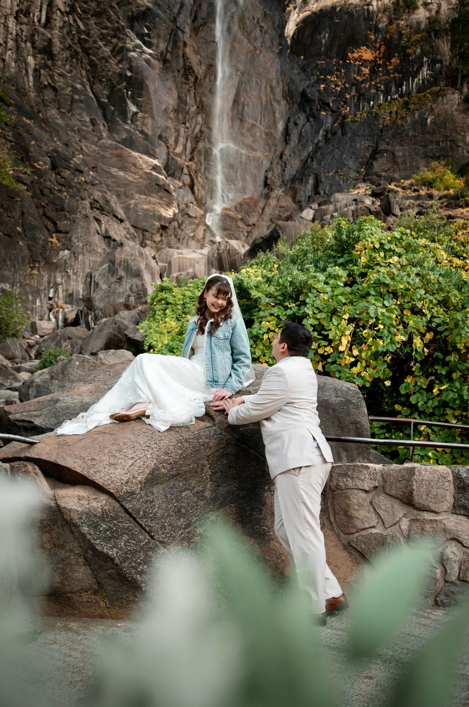 A bride and groom resting on a rock at Bridalveil falls, Yosemite