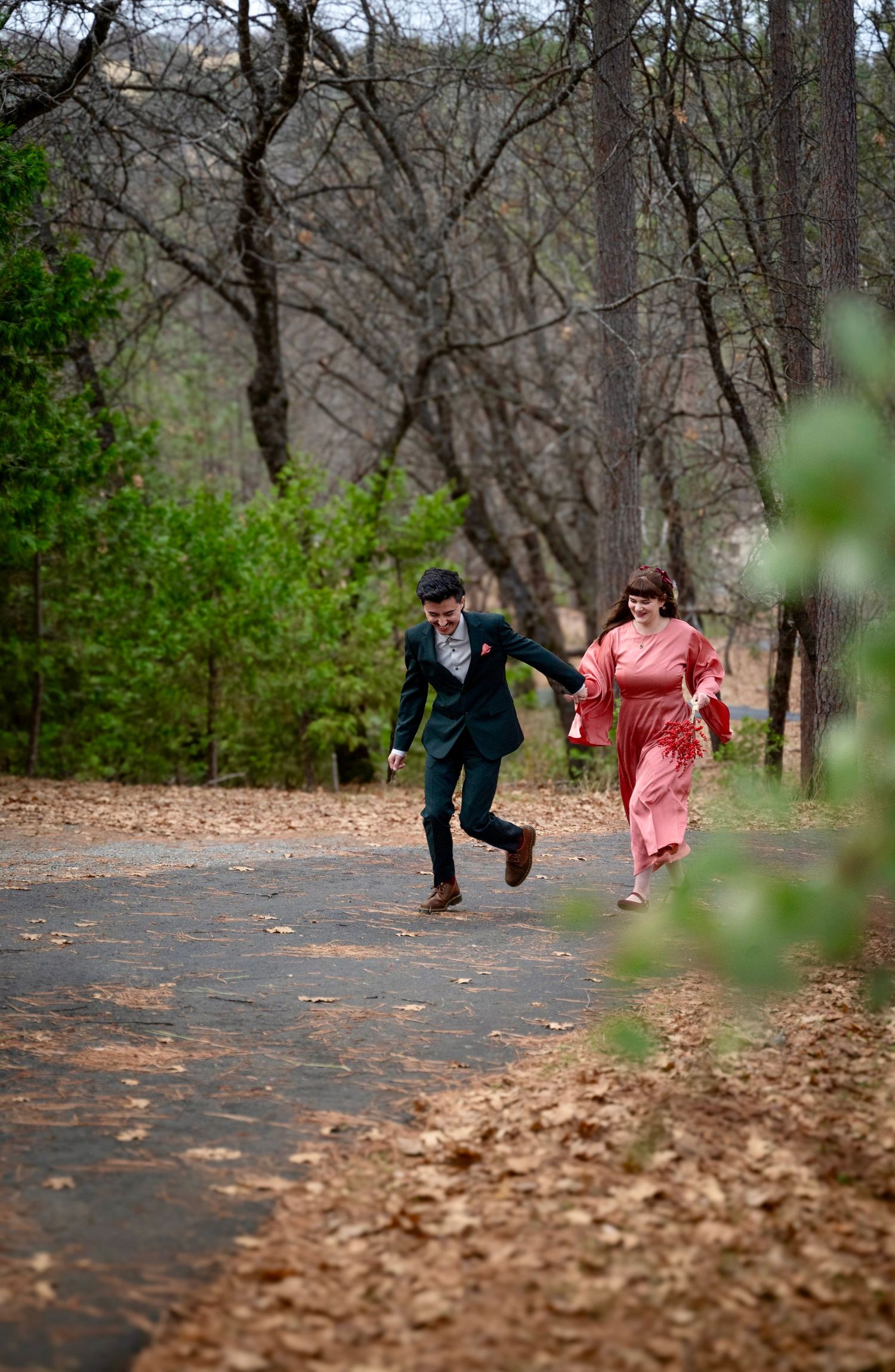 A bride and groom run together up a forest path
