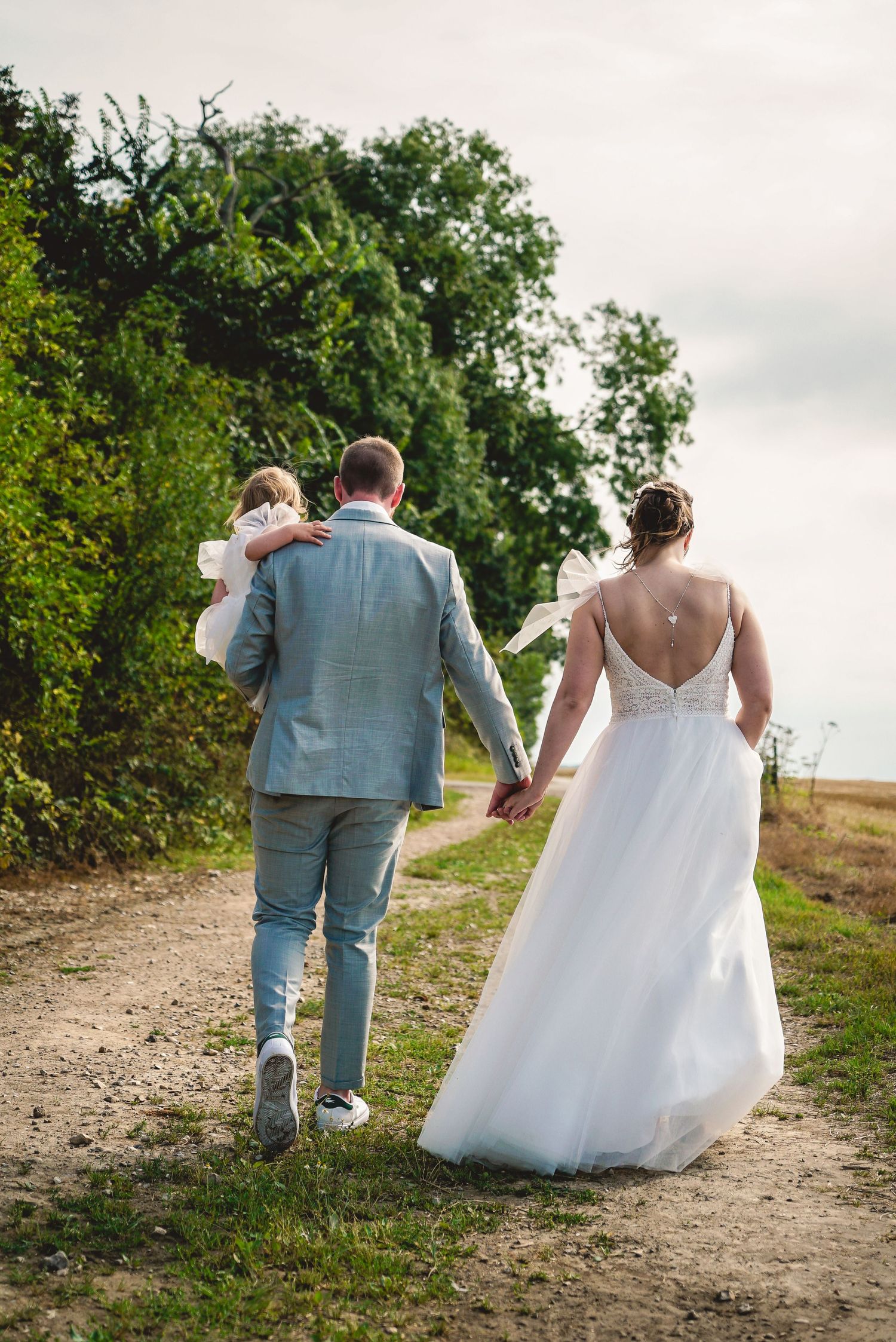 A couple walks down a dirt path together on their wedding day with lush greenery in the background.