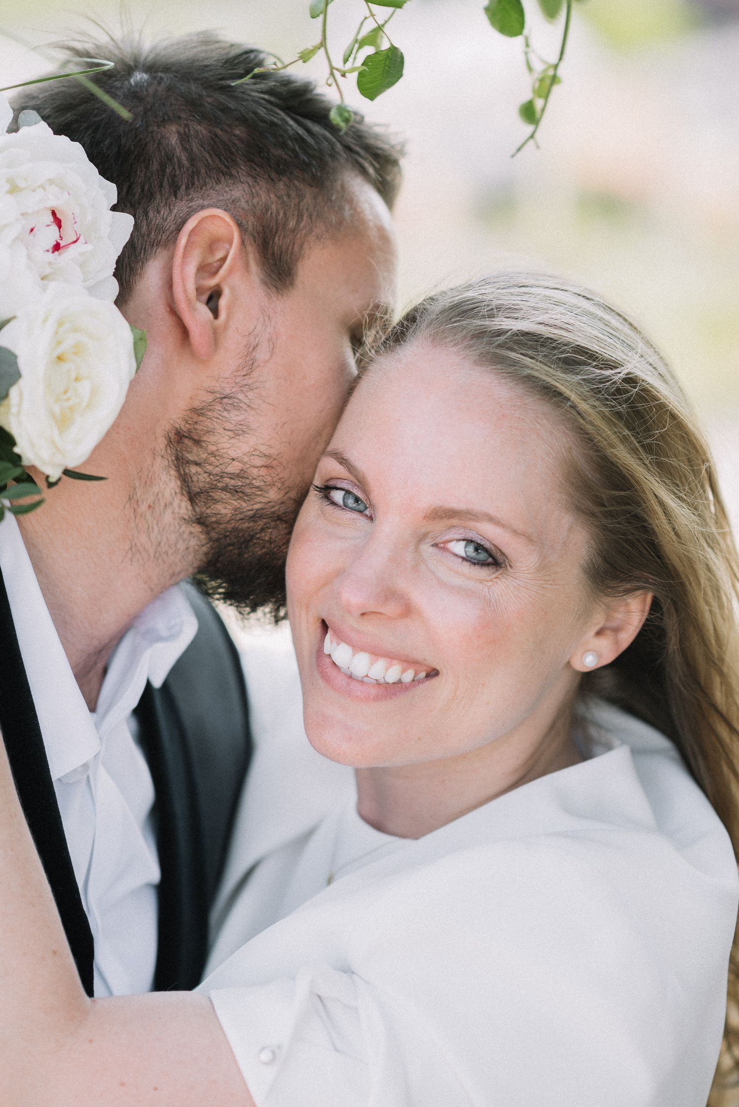 A close-up romantic wedding portrait outdoors with white roses and natural lighting.