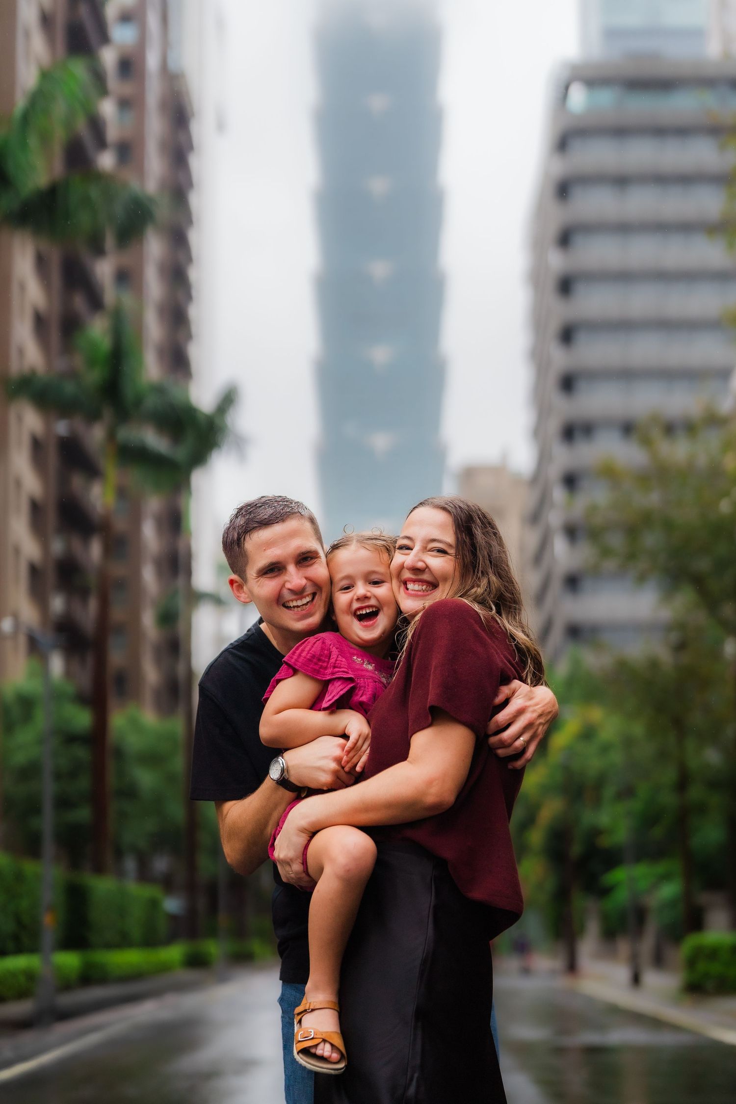 A family sharing laughter together on a rainy city street with skyscrapers in the background.