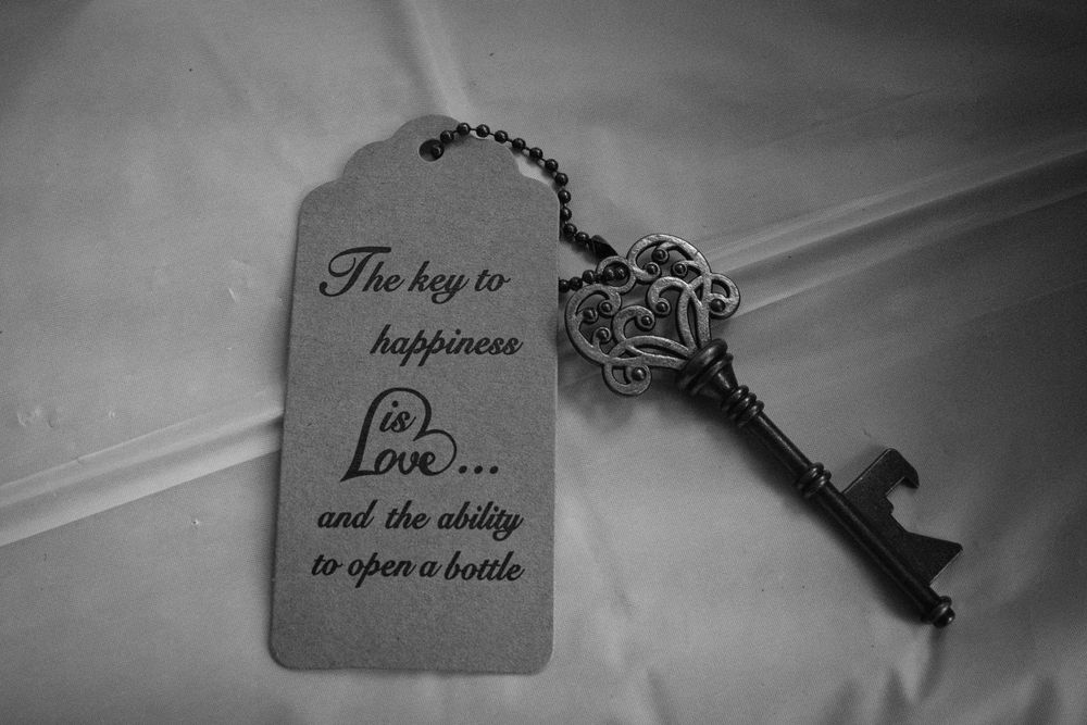 Black and white photo of a decorative skeleton key beside a tag reading the key to happiness is love and the ability to open a bottle.