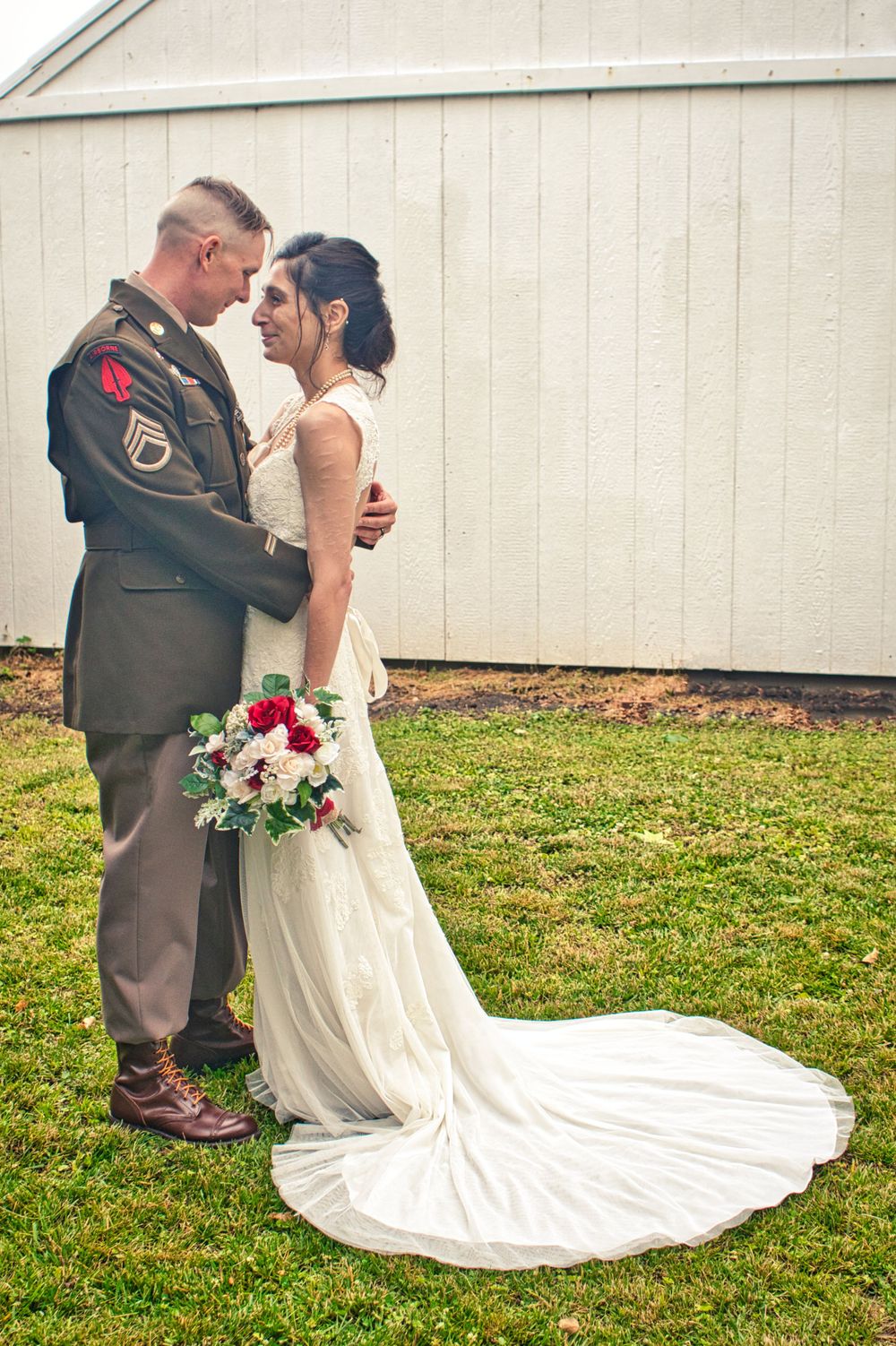 Military wedding couple in uniform and white dress share intimate moment against white building.