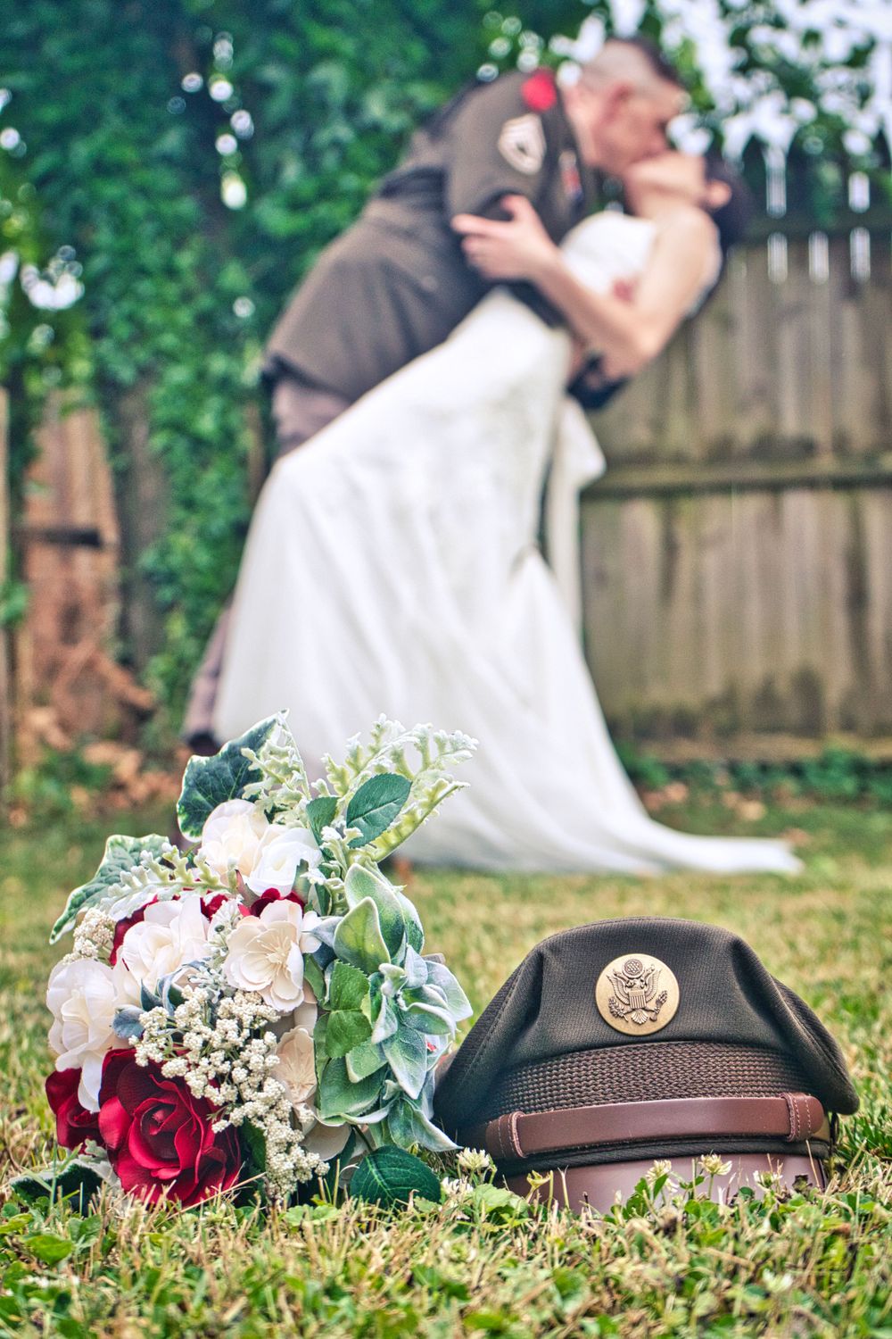 Wedding bouquet and military cap in foreground with romantic couple blurred in background.