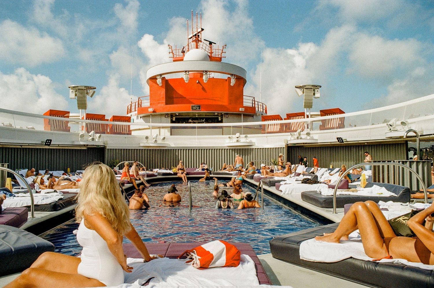 Vintage-style photo of people relaxing on deck chairs around a cruise ship pool.