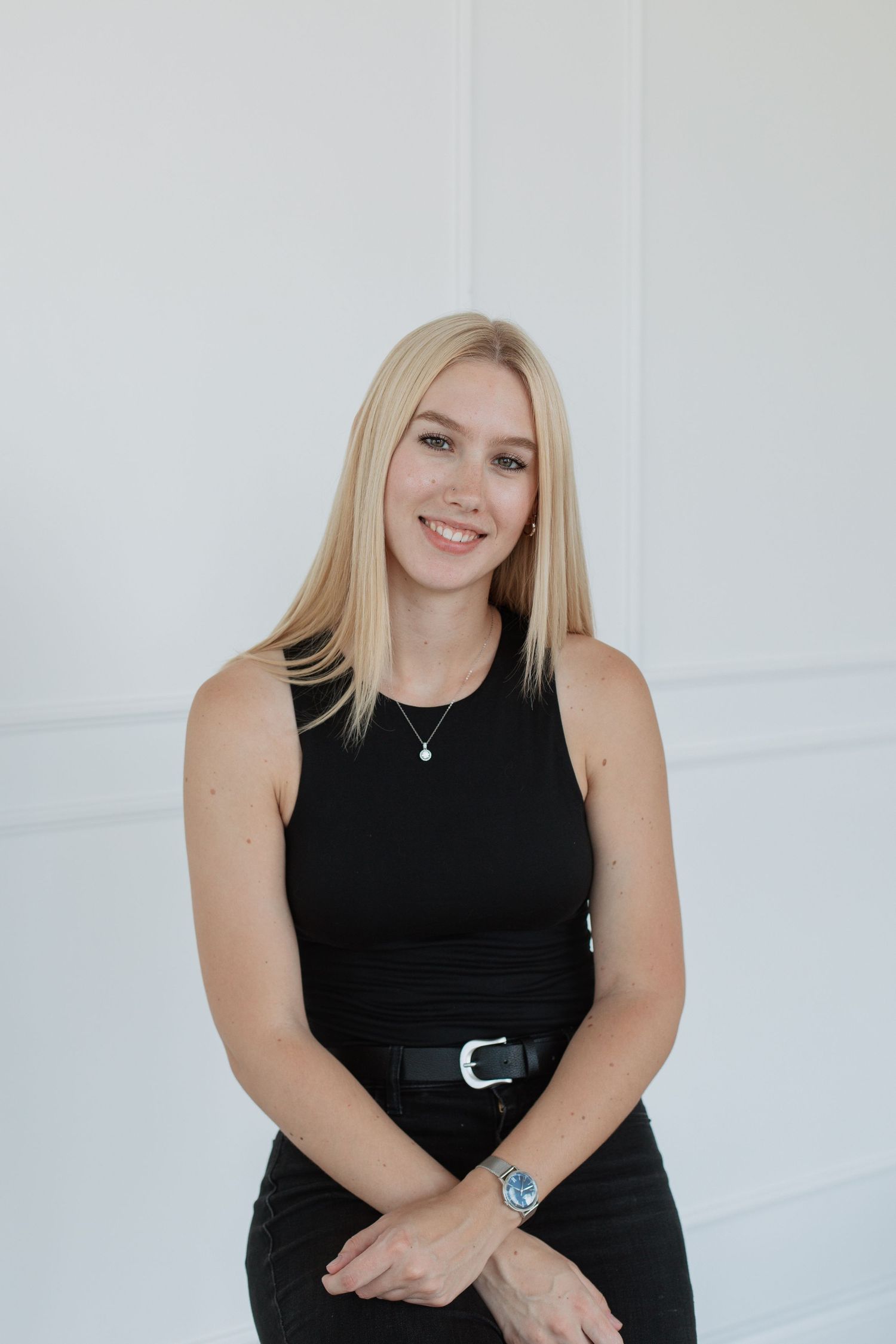Professional portrait against white wall showing sleek black outfit with silver accessories.