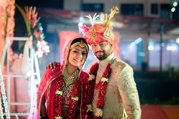 Traditional Indian wedding ceremony with vibrant red and gold attire in an indoor venue with string lights.